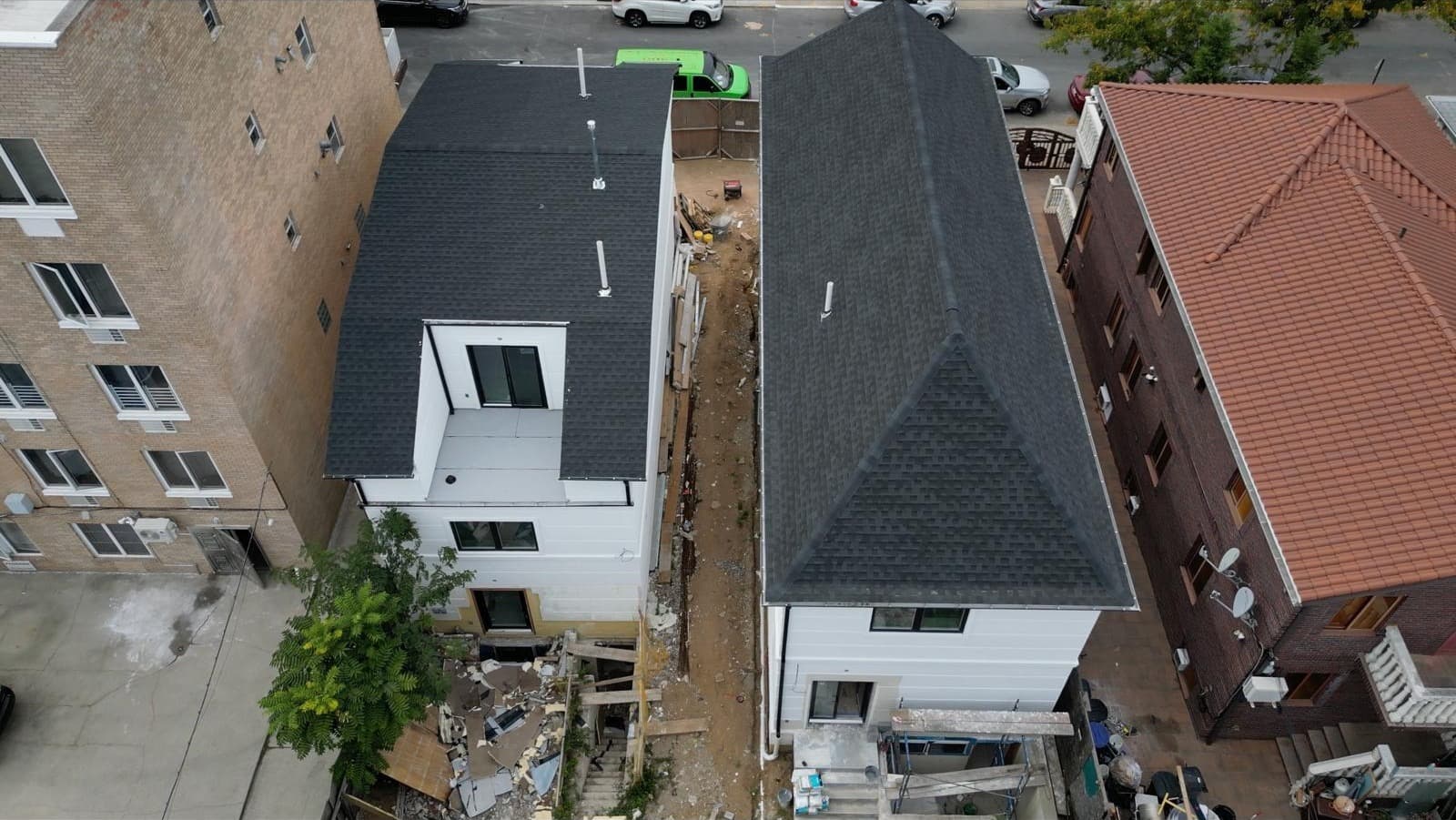 Aerial view of completed dark shingle hip roof on white Brooklyn three-story home